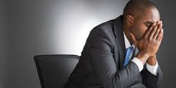 Man in suit stressed with face in hands, sitting on chair.