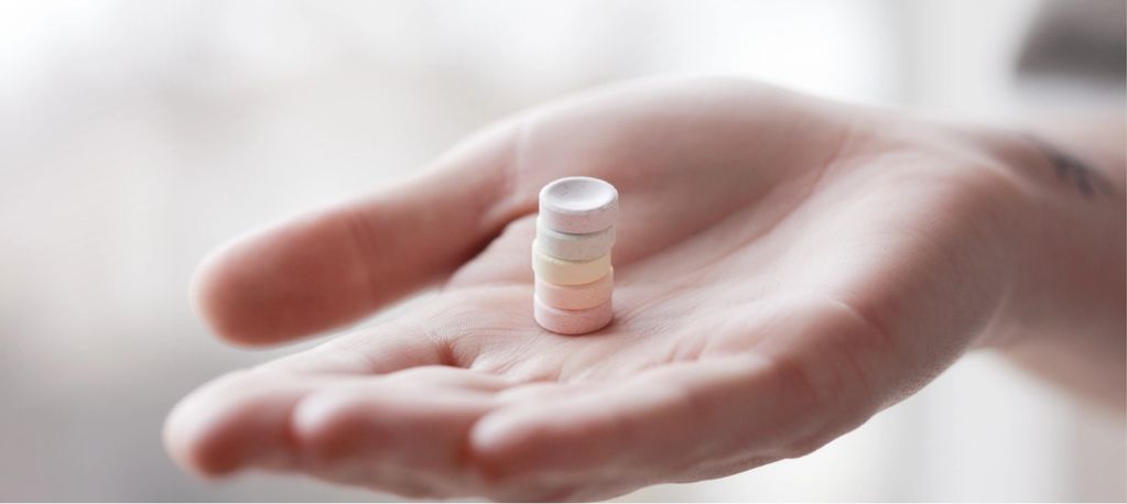Hand holding five pills stacked upon each other 