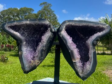 Purple geode crystals cut in half, displayed outdoors on a stand.