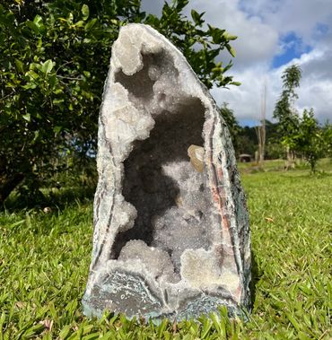 Large geode with sparkling crystals inside, standing on grass.