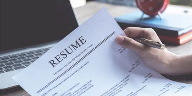 Person reviewing a resume with a laptop and clock in the background.