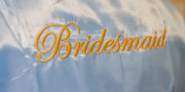 White fabric with "Bridesmaid" embroidered in yellow script.