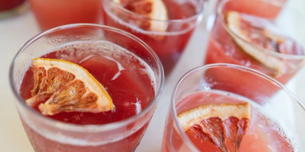 Glasses filled with iced red beverage garnished with dried citrus slices.