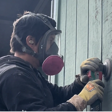 painter sanding siding on a house