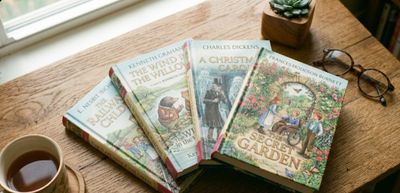 Four classic children's hardback books fanned across a wooden table: The Secret Garden, A Christmas 