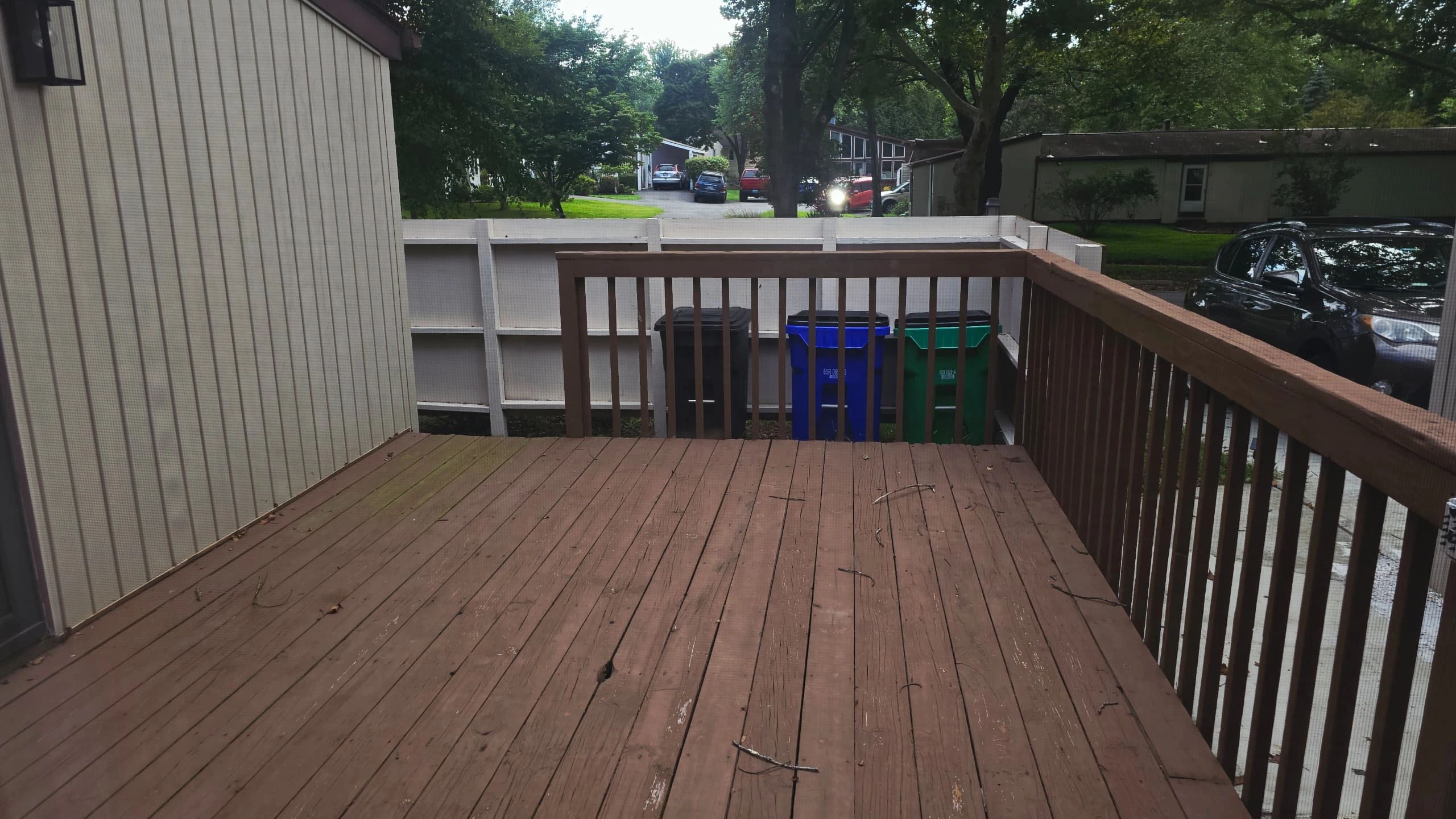 Empty wooden deck with trash bins and parked car.