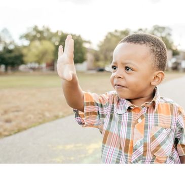 Young boy waving outdoors on a sunny day.