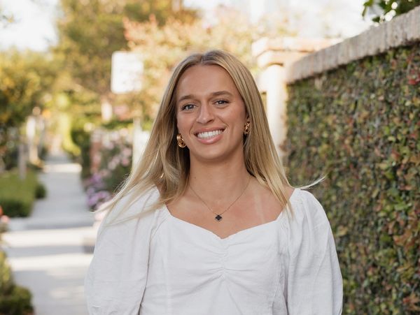 Smiling woman with blonde hair wearing a white top outdoors.