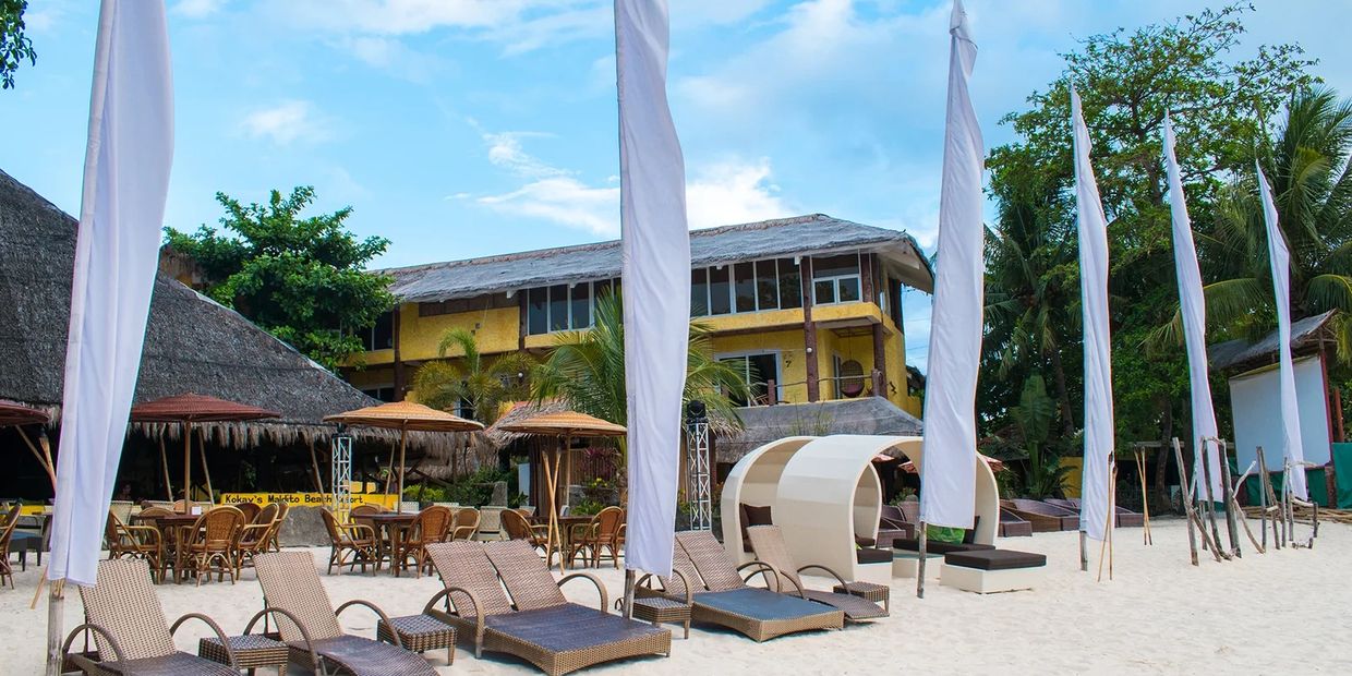 Beach resort with lounge chairs and umbrellas on white sand under a blue sky.