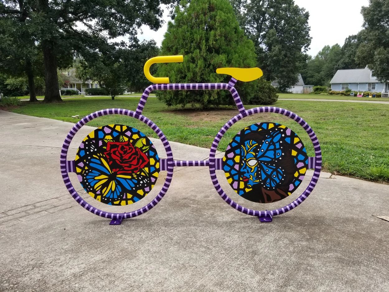 Artistic purple bike sculpture with vibrant stained glass designs.