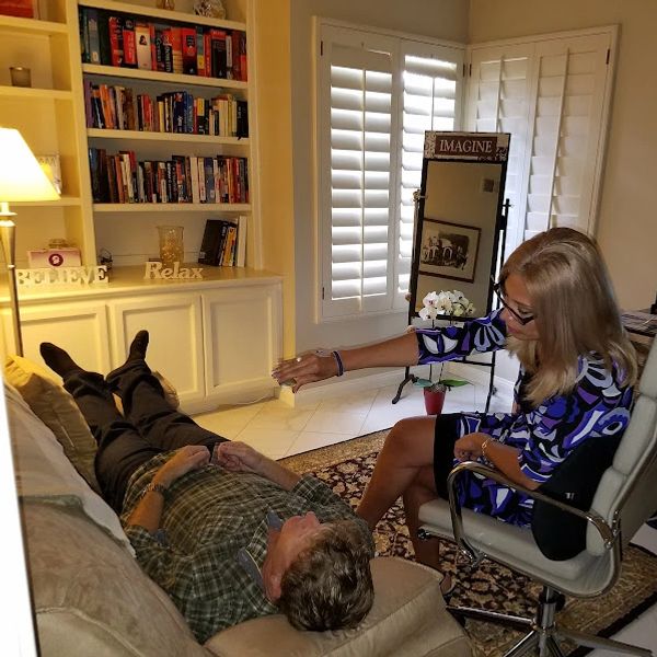 A woman comforts a man lying on a couch in a cozy living room.