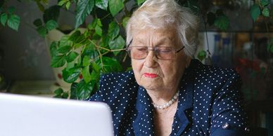 Elderly woman with clear framed glasses  sitting in front of her laptop