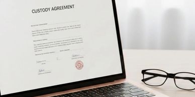 A laptop on a desk displaying a digital custody agreement with a pair of glasses nearby