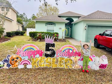 A young child celebrates their 5th birthday with a colorful yard sign display.