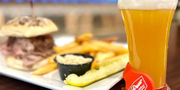 Burger, fries, pickle, and a glass of beer on a white plate.