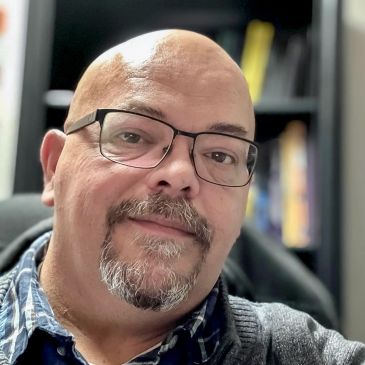 A man with glasses and a goatee smiling gently at the camera.