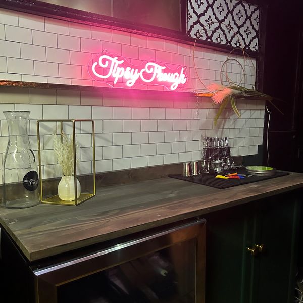 Cozy bar counter with neon "Tipsy Frogs" sign and stylish decor.