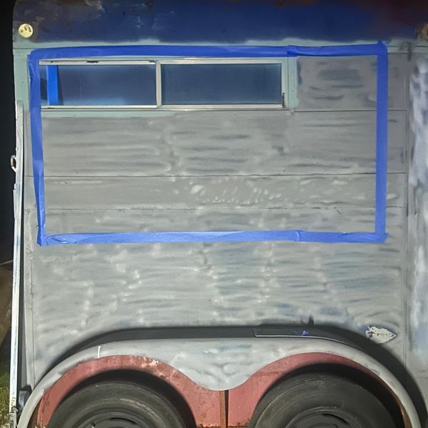 Trailer wall with taped window outline and wheels visible at the bottom.