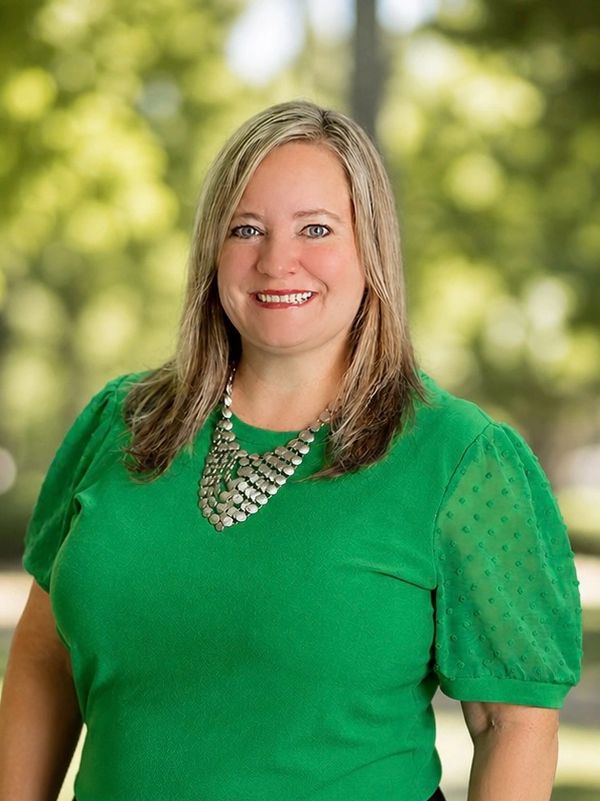 Smiling woman in green top with a statement necklace outdoors.