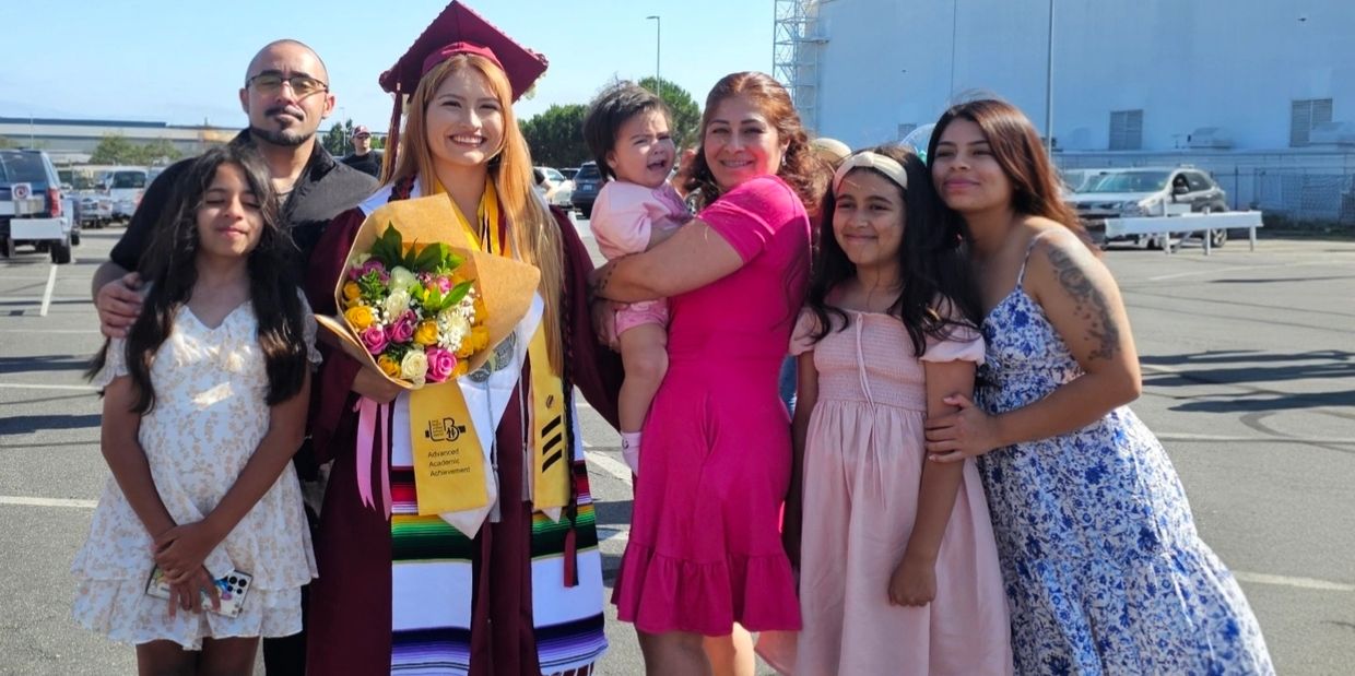 A joyful graduate with family celebrating outdoors in a sunny parking lot.