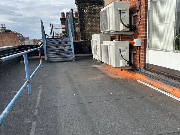 Rooftop with metal staircase, air conditioning units, and chimney stacks under a cloudy sky.
