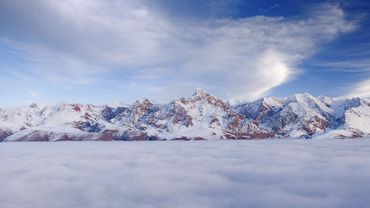 Snow-covered mountain range above a sea of clouds under a blue sky.