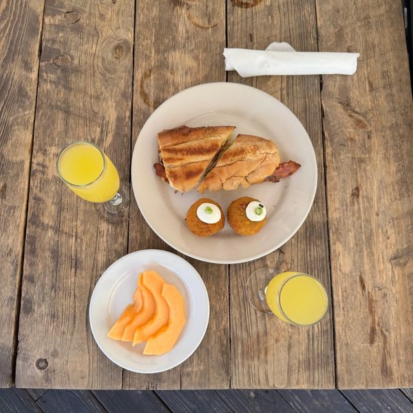 Breakfast with sandwich, fried balls, cantaloupe, and orange juice.