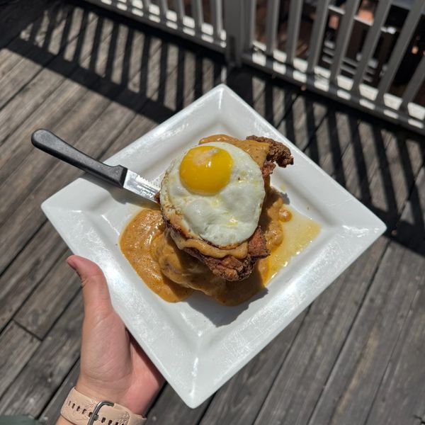 Fried egg on top of a breaded dish with sauce on a white plate.