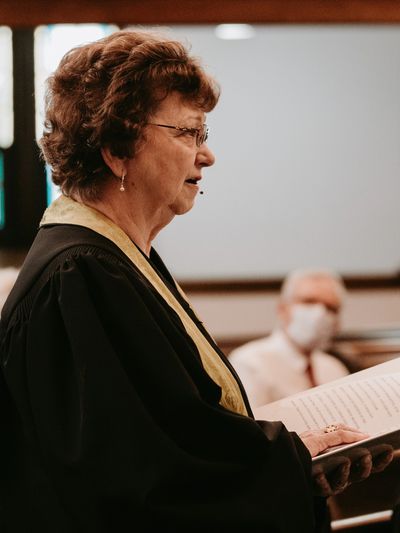 A woman in religious attire reads from a book during a service.