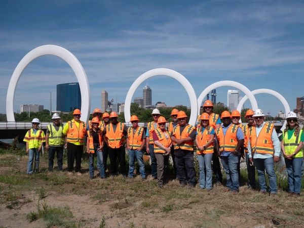 Group of construction workers in safety gear near modern bridge.