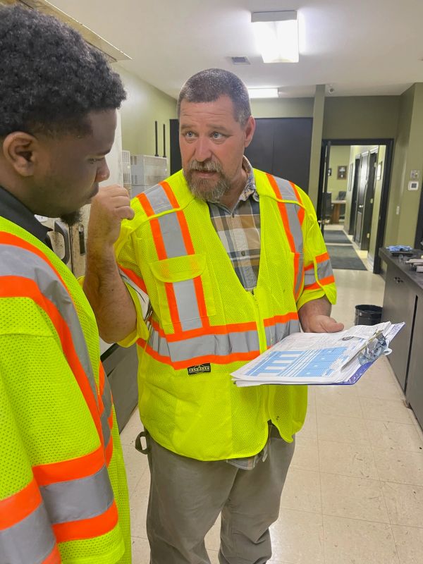 Two workers discussing plans indoors wearing safety vests.