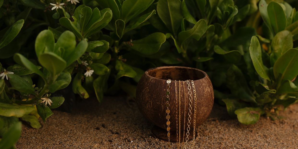 a Hawaii coconut holding permanent jewelry chains in 14k gold