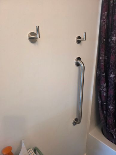 Bathroom wall with hooks and a grab bar next to a bathtub.