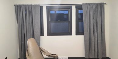 Room with gray curtains, wooden floor, and a beige reclining chair.