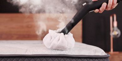 Steaming a mattress with a handheld garment steamer and cloth.
