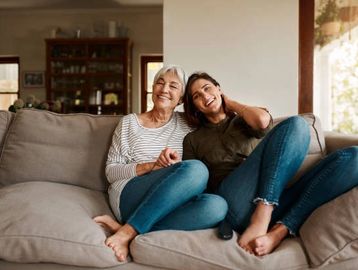 Two women sitting comfortably on a couch, smiling and enjoying each other's company.