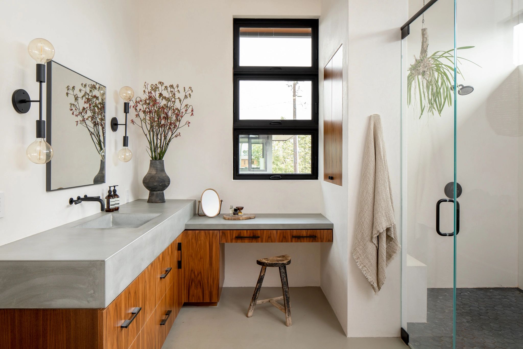 Modern bathroom with wood cabinetry, concrete countertops, and large window.