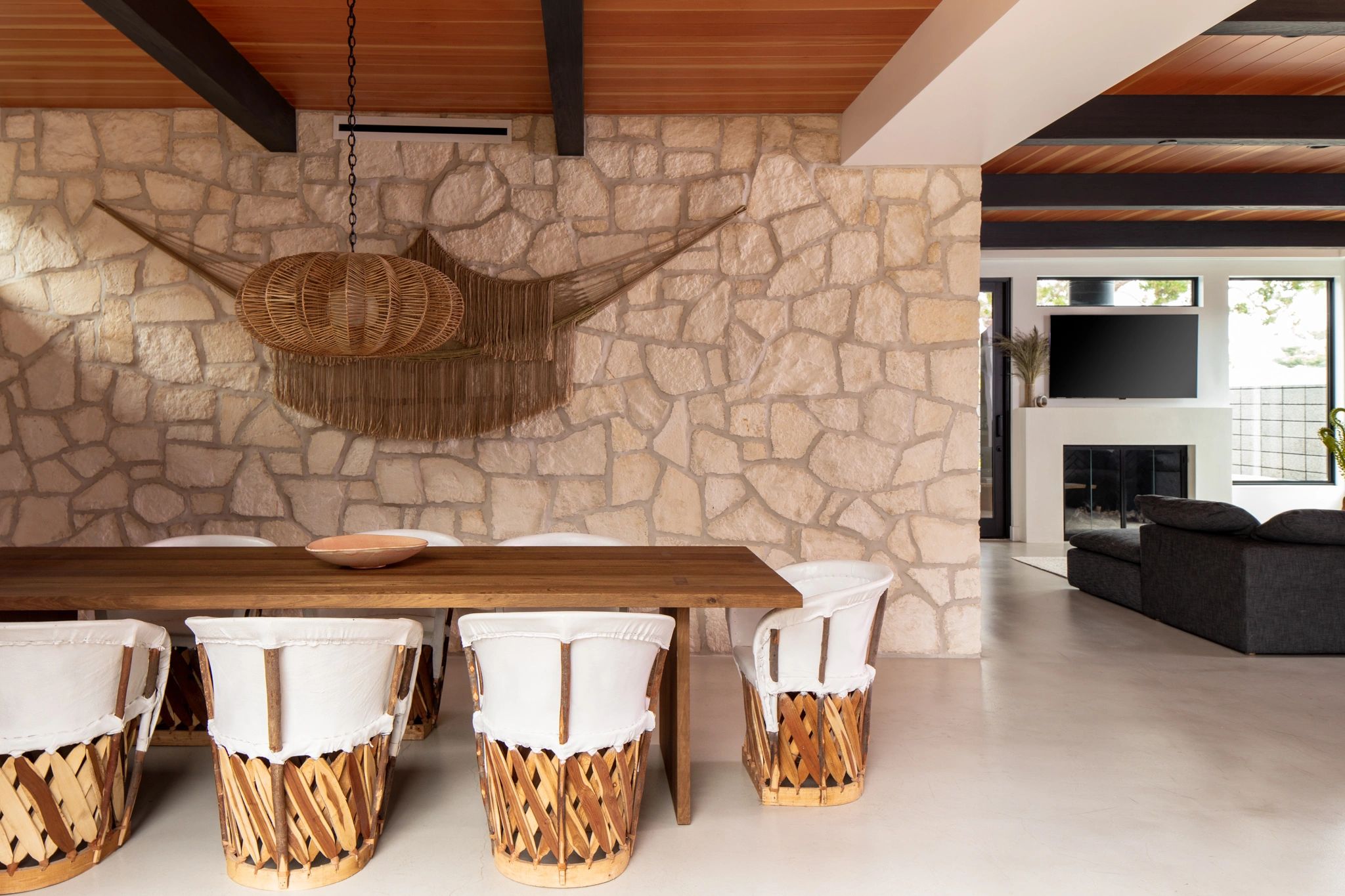 Rustic dining area with woven chairs and stone wall.