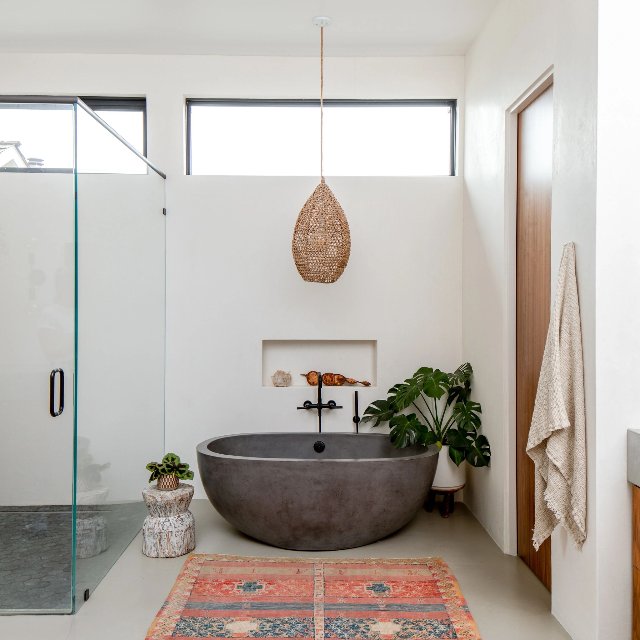 Modern bathroom with a concrete bathtub and woven pendant light.