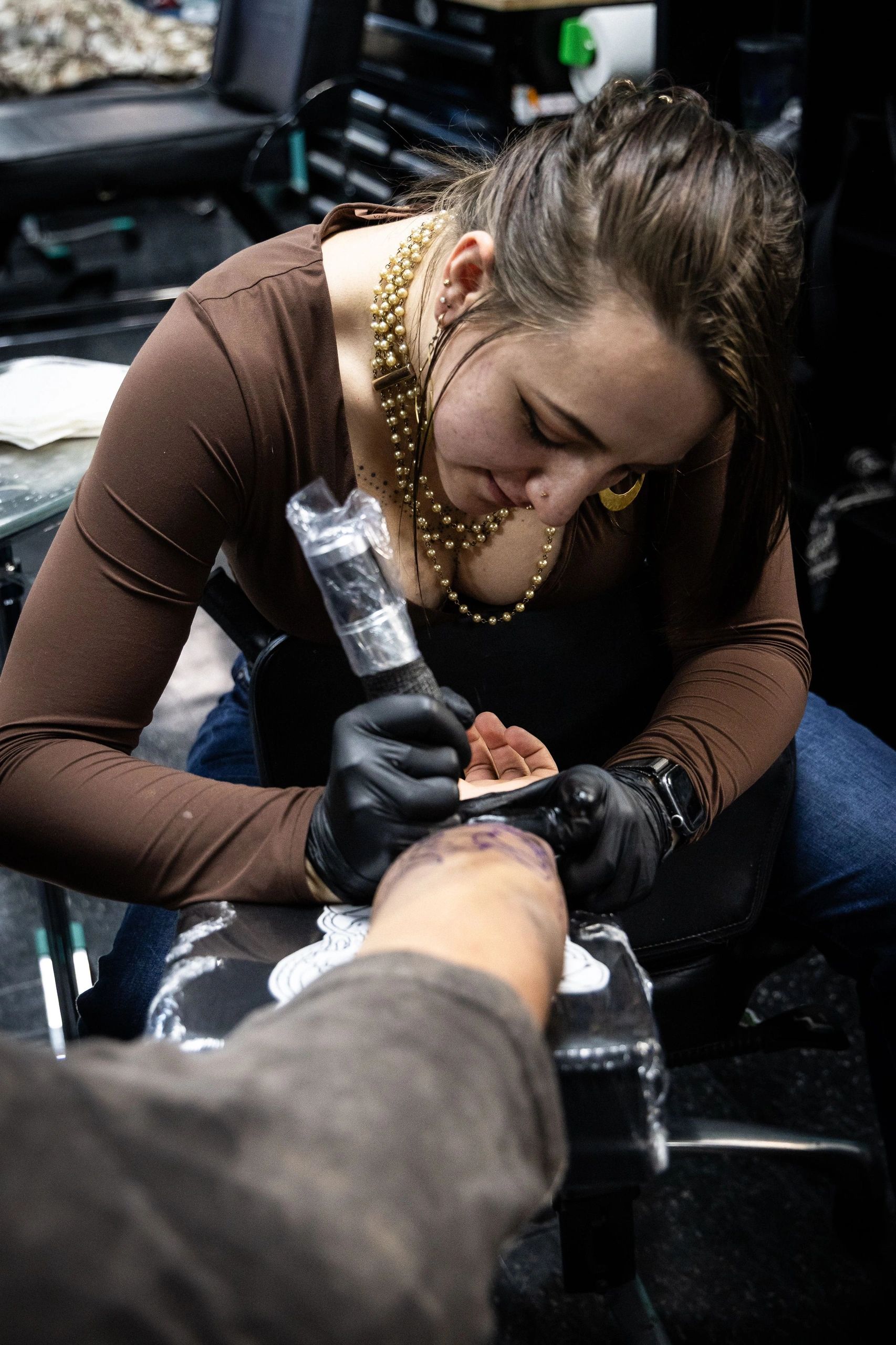 A woman tattoo artist inking a person's arm.
