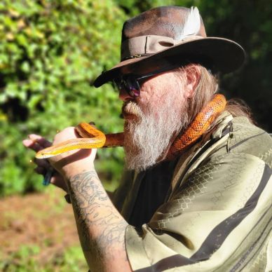 Man with a beard and hat holding a snake.
