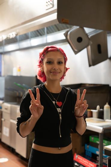 A woman with red hair making peace signs in a kitchen.