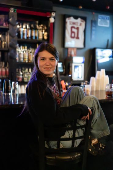 A young woman sitting on a bar stool, smiling at the camera.