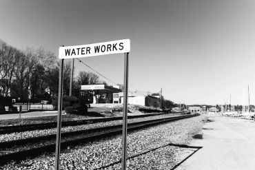 Black and white image of a railroad track with a 'Water Works' sign beside it.