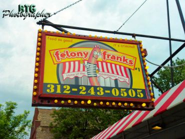 Colorful sign for Felony Franks hot dog stand with phone number and lights.