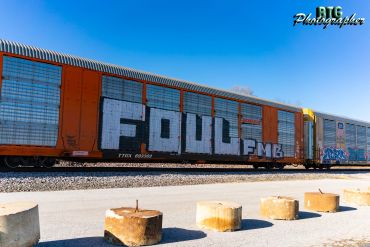 Graffiti 'FOUL' painted on an orange train car under a clear blue sky.