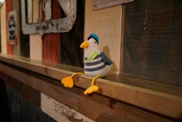 A plush seagull toy with a blue hat sitting on a wooden ledge indoors.