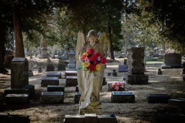 A stone angel statue holding colorful flowers in a cemetery.
