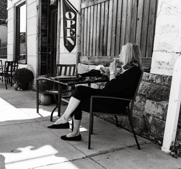 Woman sitting outside a cafe under an 'OPEN' sign.