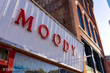 Red "MOODY" letters on a white storefront against a brick building.